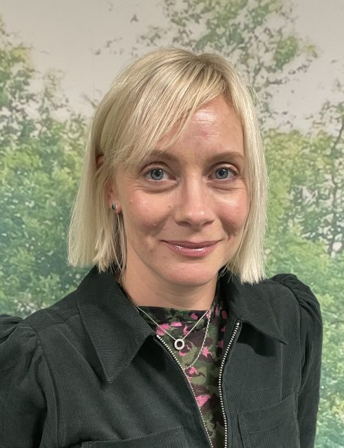Emma against a greenery background, smiling at the camera