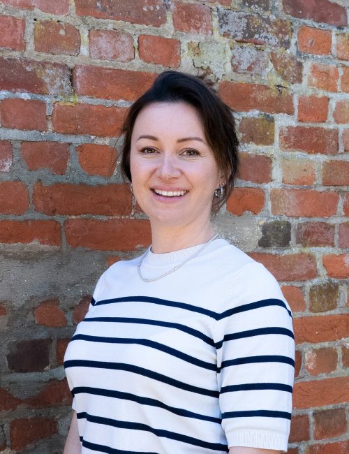 Kirsten against a brick wall, smiling at the camera